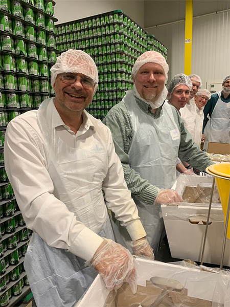 Community Involvement - Team Smiling and Lined Up Volunteering With Hairnets and Gloves